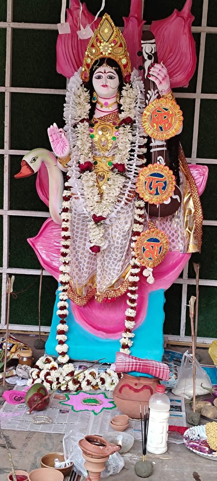 Saraswati idol seated on a lotus with a swan, decorated with garlands and puja offerings laid out in front